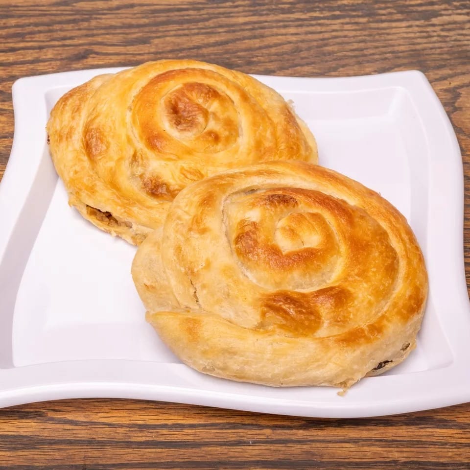 Two golden-brown spiral pastries on a white rectangular plate, against a dark wooden background.
