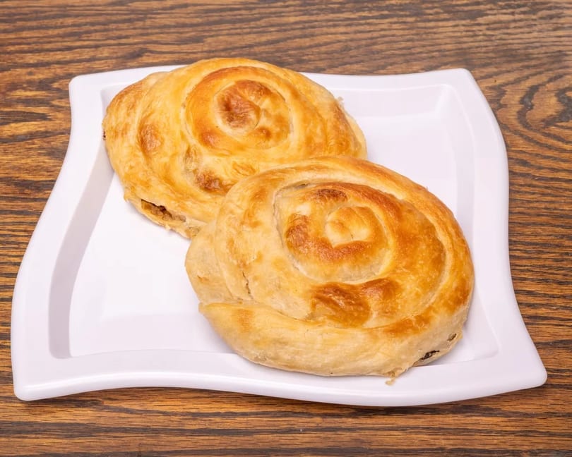 Two golden-brown spiral pastries on a white rectangular plate, against a dark wooden background.