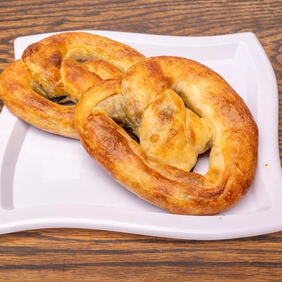 Two golden-brown, twisted pastries on a white rectangular plate, set against a wooden table.