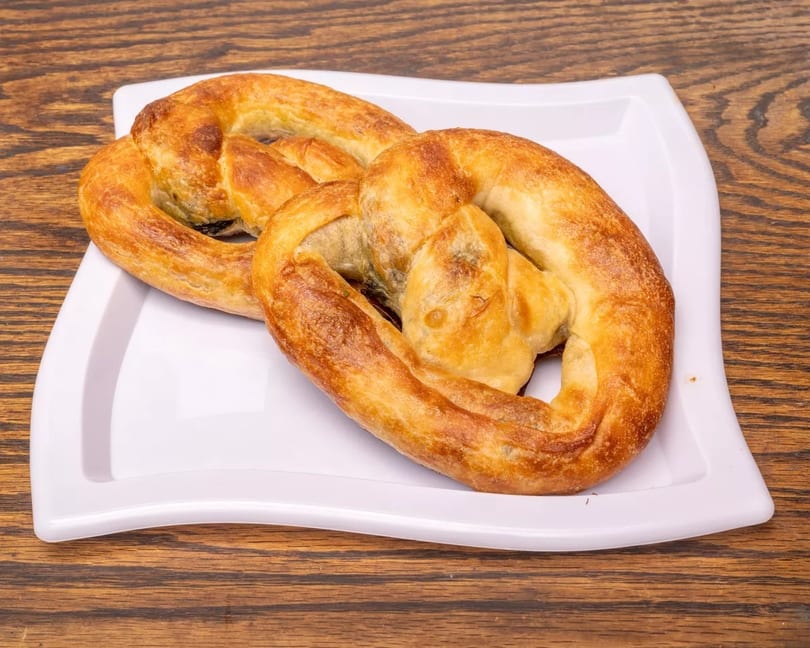 Two golden-brown, twisted pastries on a white rectangular plate, set against a wooden table.