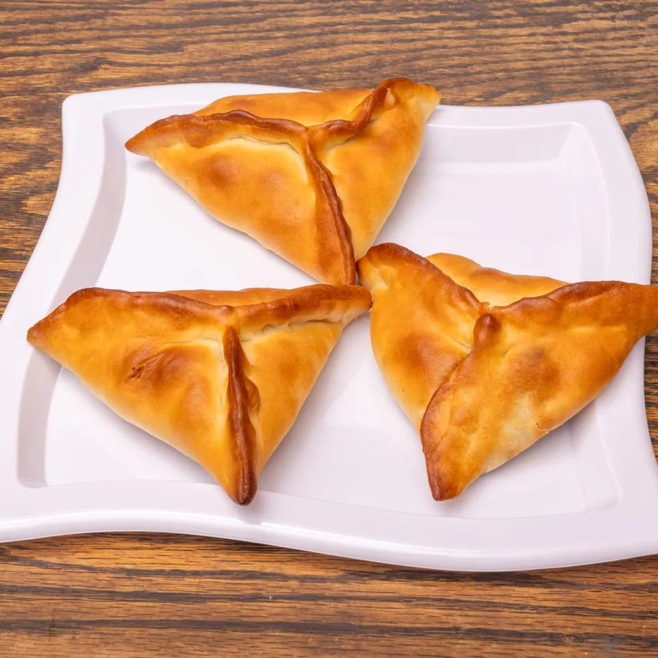 Three golden-brown, triangular pastries with crimped edges on a white plate against a wooden background.