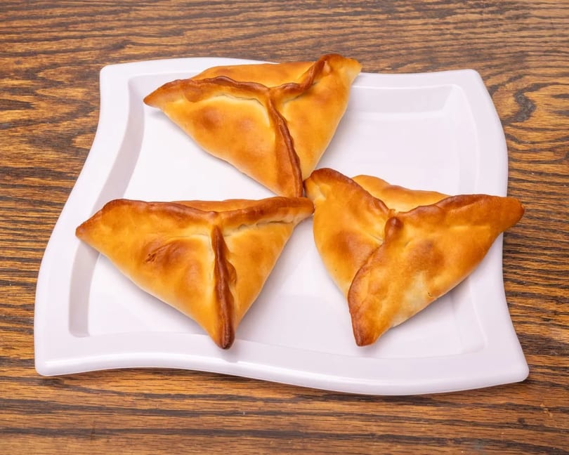 Three golden-brown, triangular pastries with crimped edges on a white plate against a wooden background.