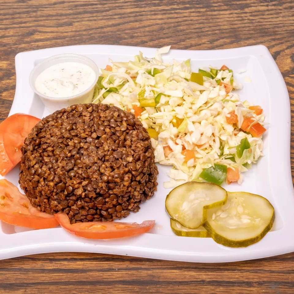 A plate of lentils, coleslaw, tomato slices, pickles, and a side of white sauce.