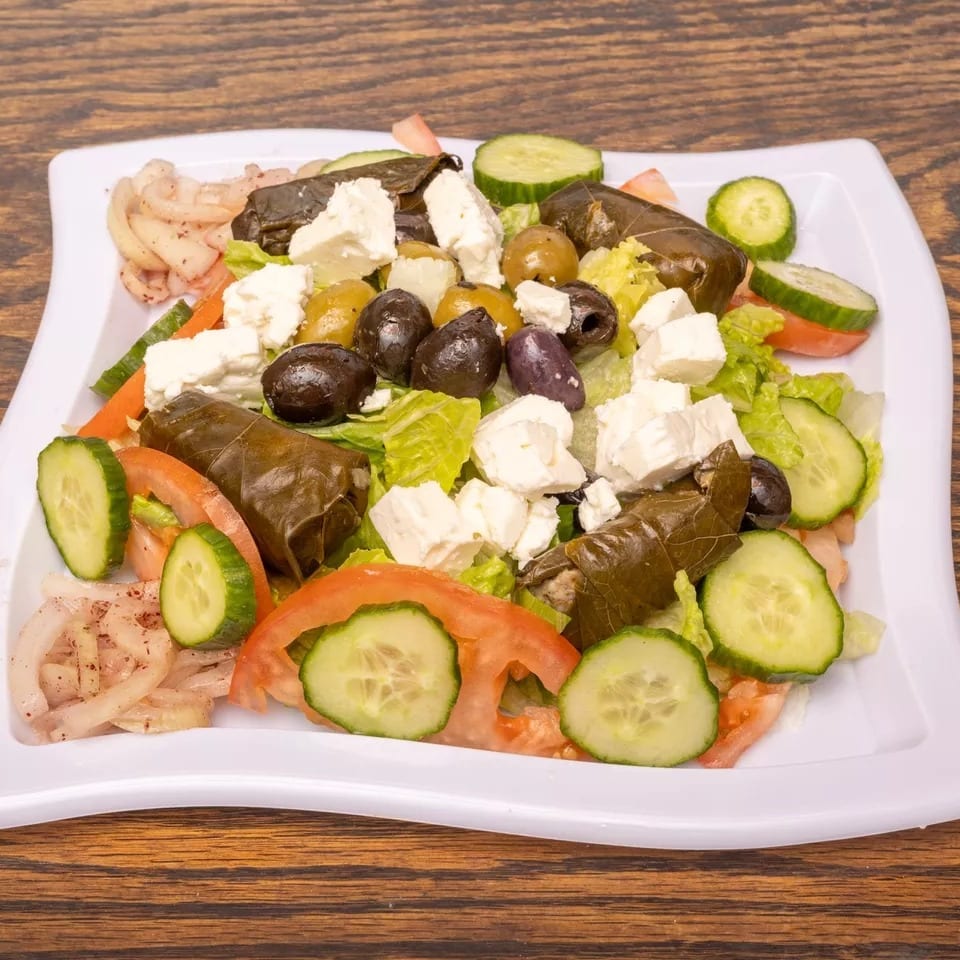 A vibrant salad with lettuce, cucumbers, tomatoes, feta, olives, and stuffed grape leaves.