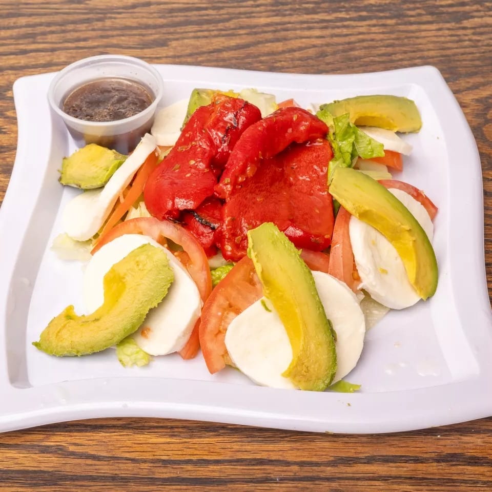 Caprese salad with sliced mozzarella, tomatoes, avocado, roasted red peppers, and dressing.
