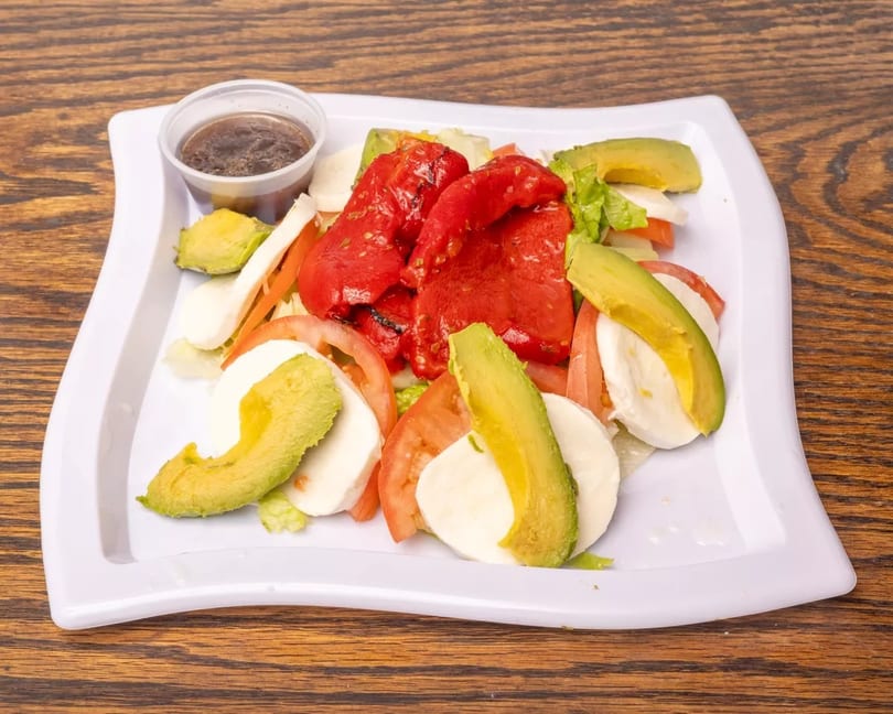 Caprese salad with sliced mozzarella, tomatoes, avocado, roasted red peppers, and dressing.