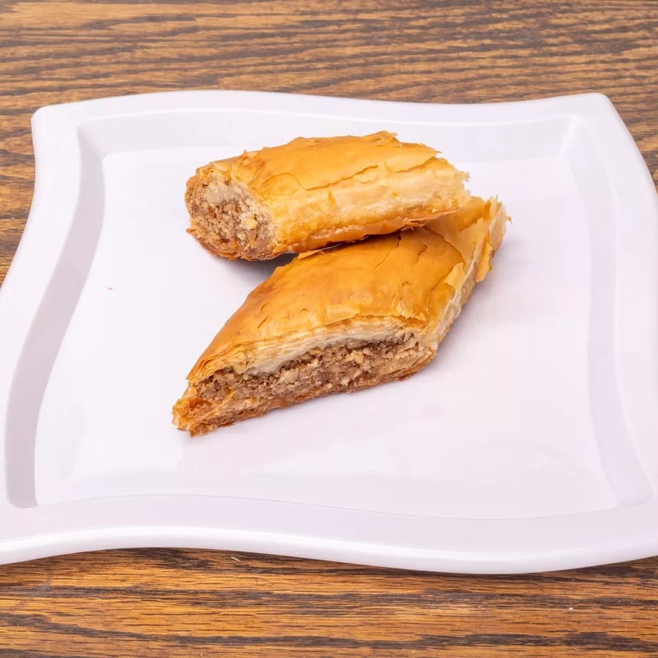 Two pieces of golden-brown baklava with nut filling on a white wavy plate.