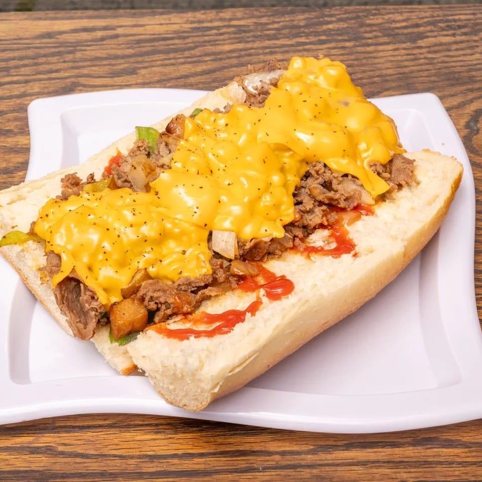 Cheesesteak sandwich with melted cheese, steak, onions, and peppers on a white plate.