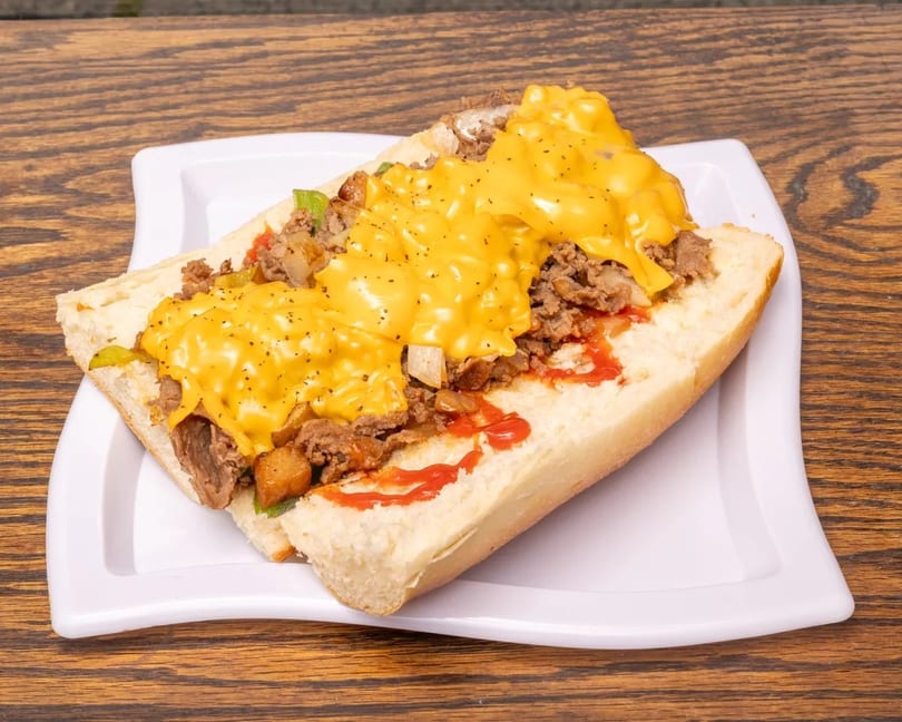 Cheesesteak sandwich with melted cheese, steak, onions, and peppers on a white plate.